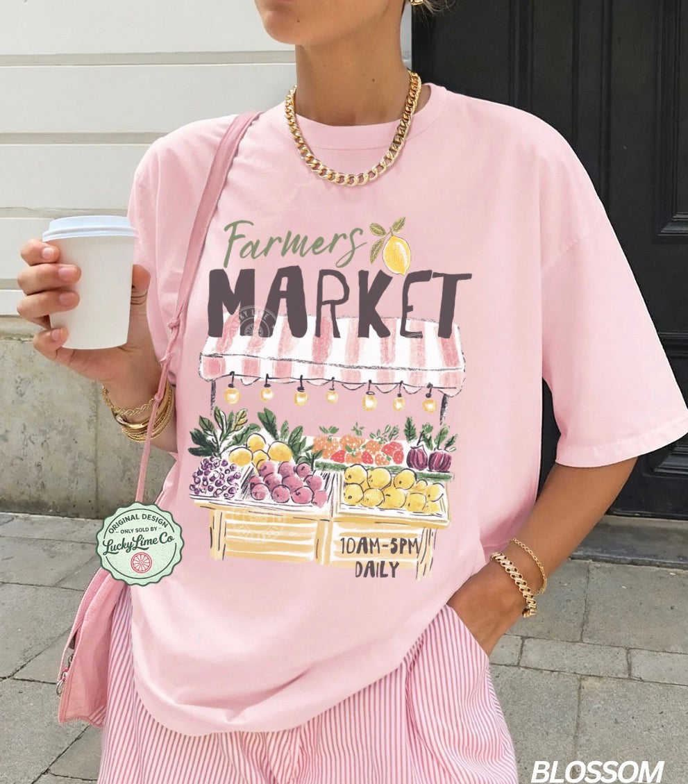 Person wearing a pink 'Farmers Market' t-shirt holding a coffee cup.