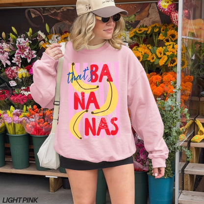 Person wearing a pink sweatshirt with colorful text and graphics, standing in front of a flower shop.