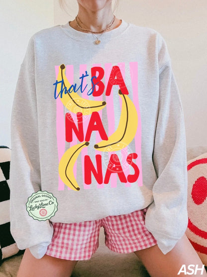 Person wearing a gray sweatshirt with colorful text and bananas, sitting on a couch.