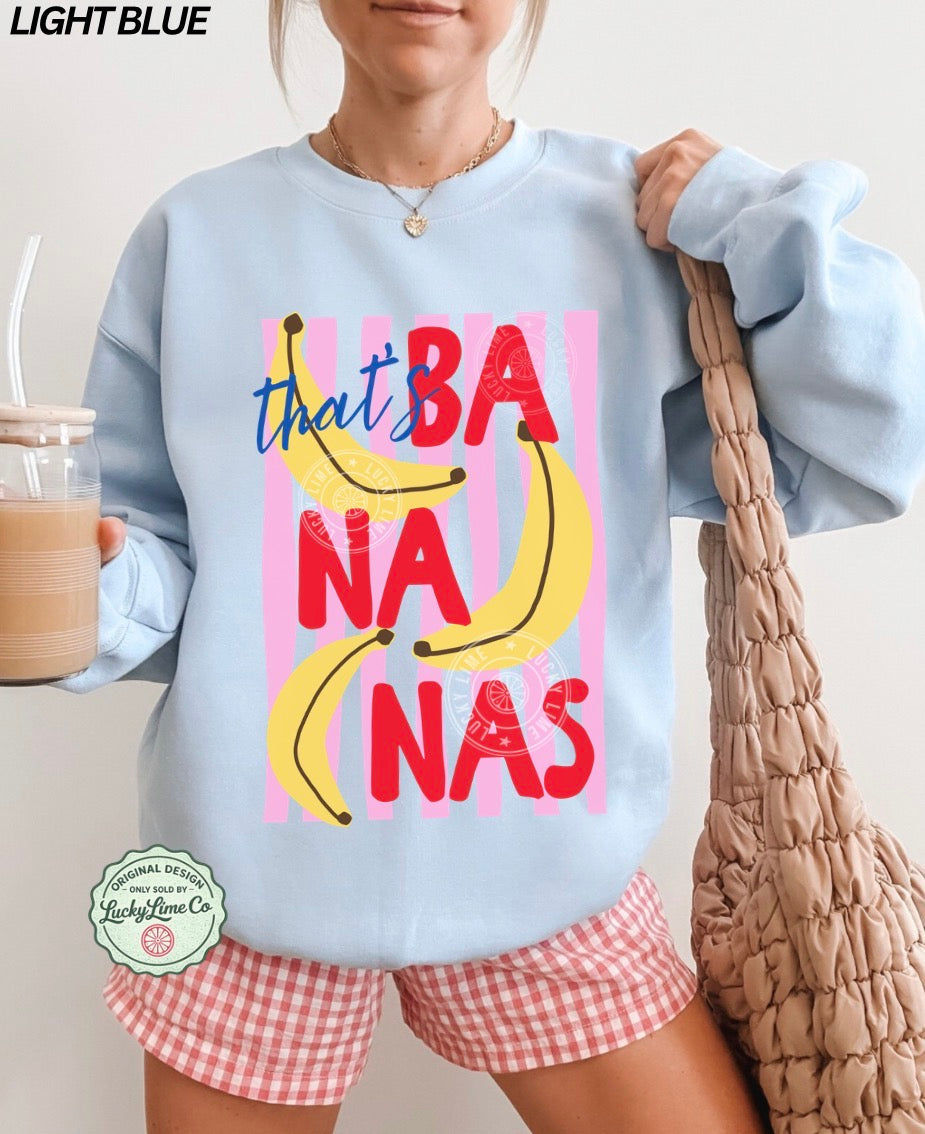 Person wearing a light blue sweatshirt with colorful text and banana graphics, holding a bag and a drink.