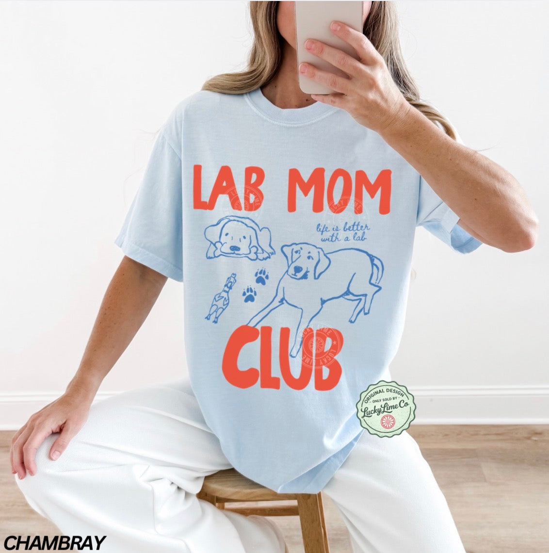 Person wearing a light blue t-shirt with 'Lab Mom Club' design, sitting on a stool.