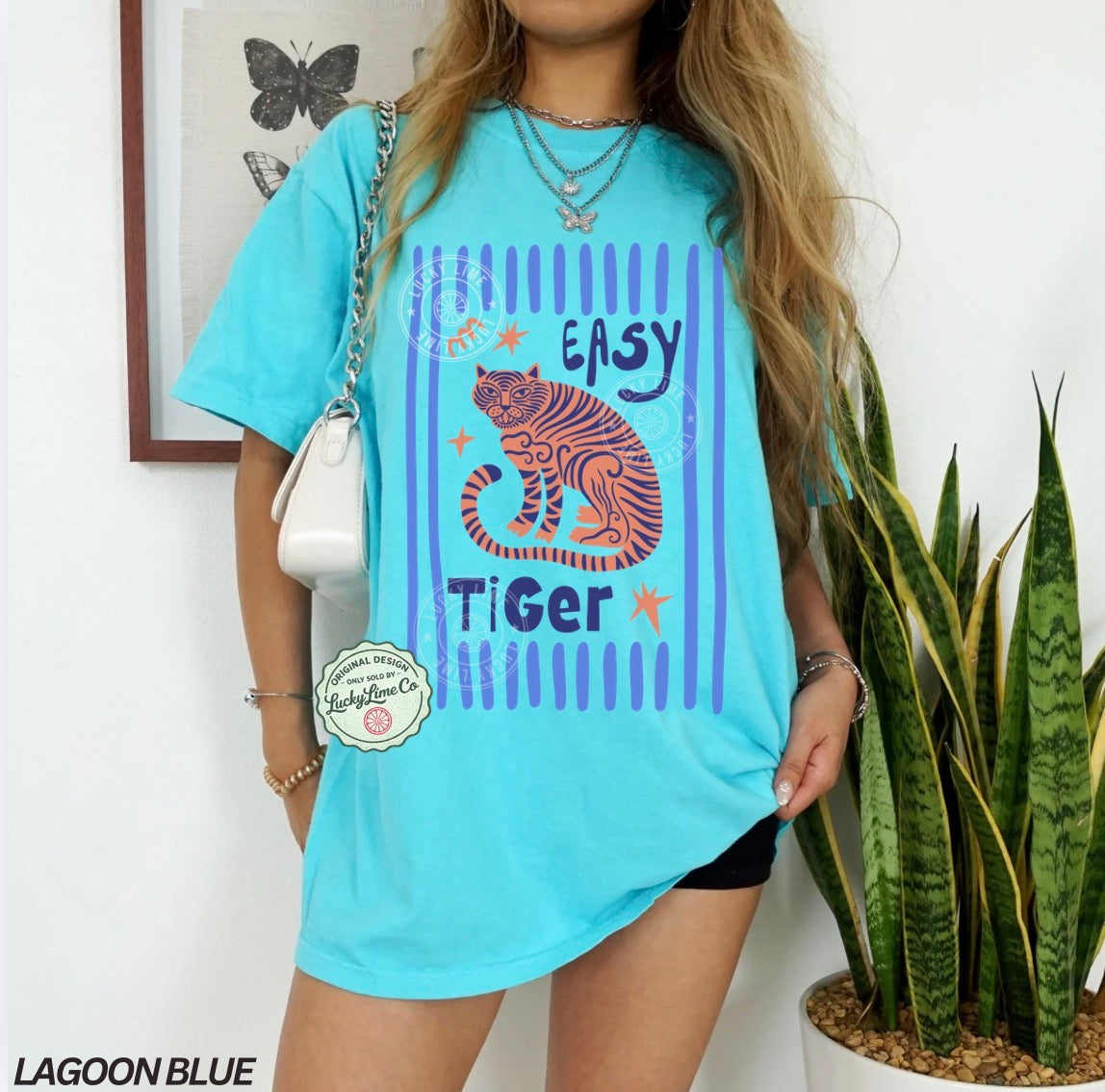 Person wearing a light blue t-shirt with a tiger graphic and text, standing next to a plant.