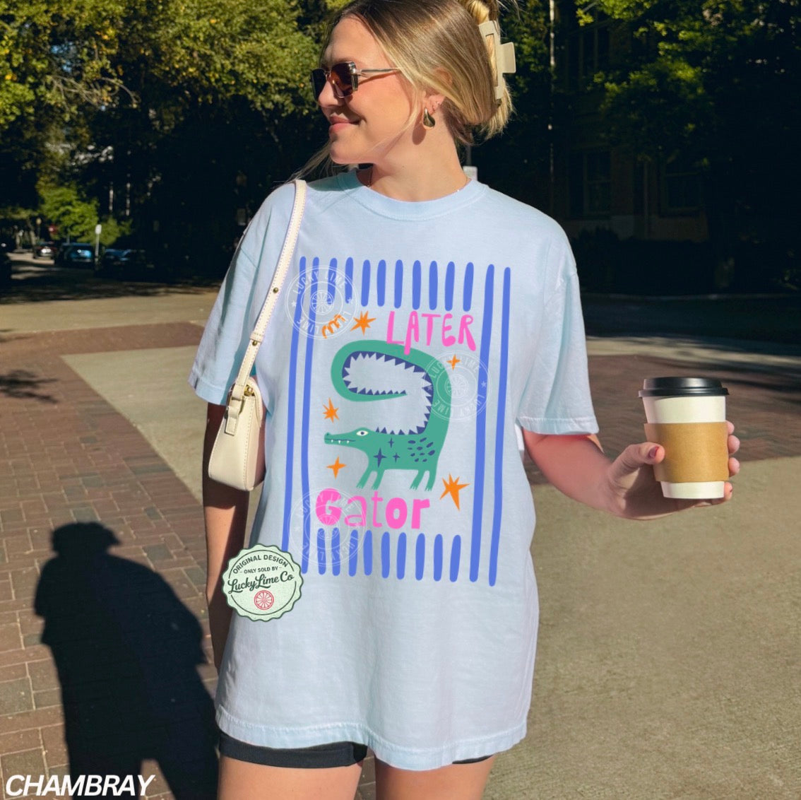 Woman wearing a light blue t-shirt with a graphic design, holding a coffee cup outdoors.