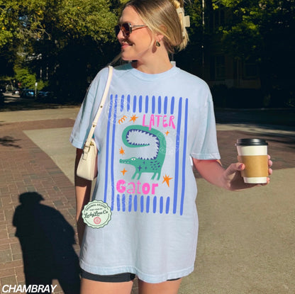 Woman wearing a light blue t-shirt with a graphic design, holding a coffee cup outdoors.