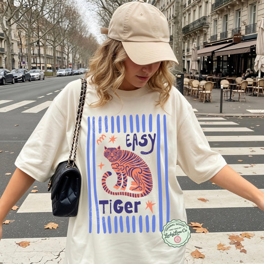Person wearing a white t-shirt with a tiger graphic and 'Easy Tiger' text on a city street.
