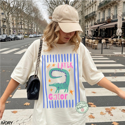 Person wearing a white t-shirt with an alligator graphic and 'LATER GATOR' text on a city street.