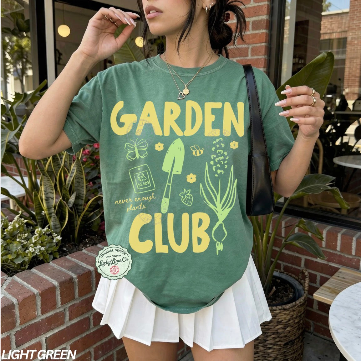 Person wearing a green 'Garden Club' t-shirt with yellow text and graphics, standing outdoors.