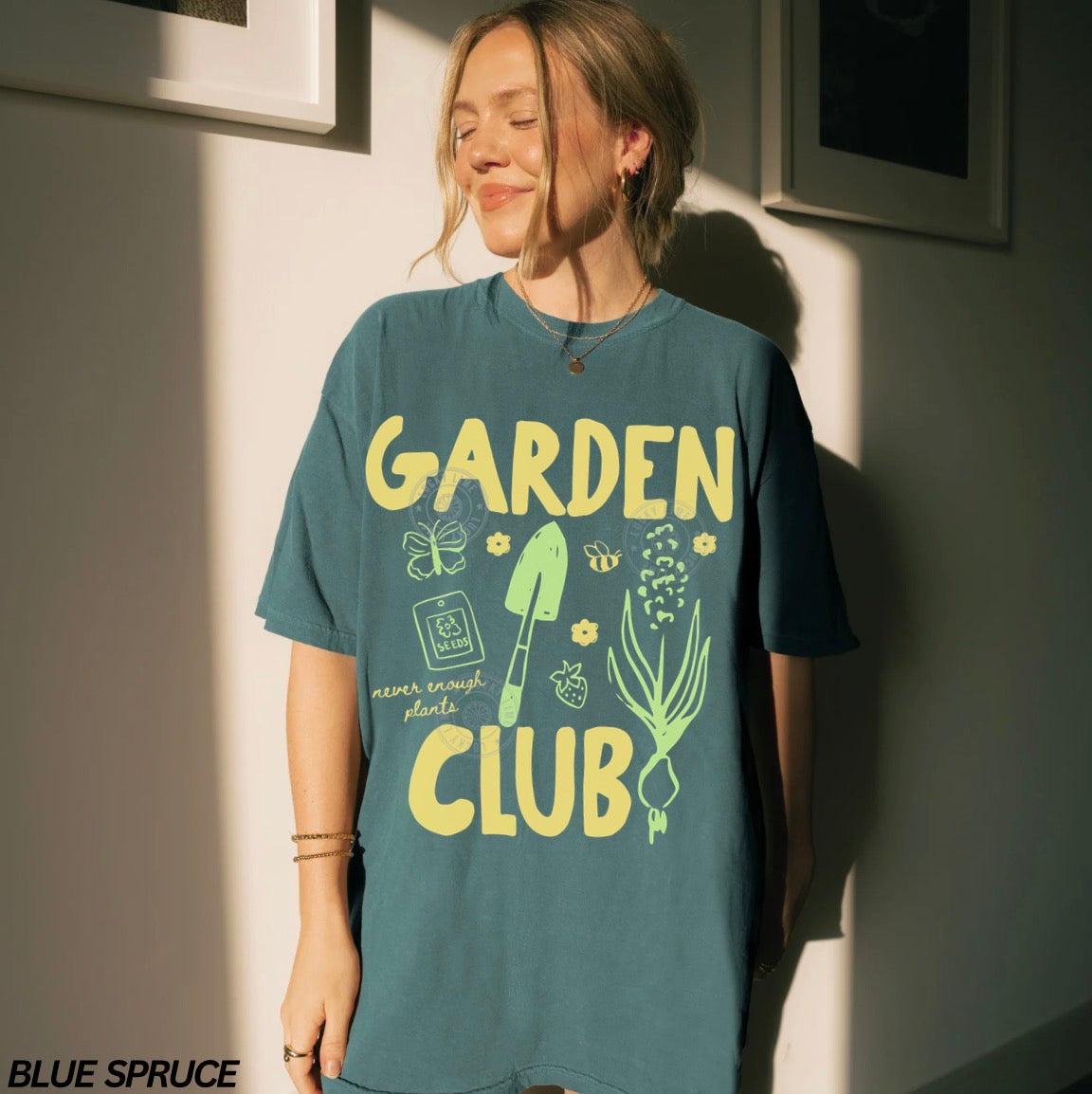 Person wearing a teal t-shirt with 'Garden Club' design, standing against a light wall.
