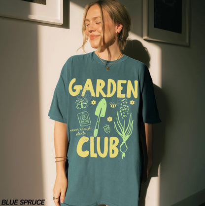 Person wearing a teal t-shirt with 'Garden Club' design, standing against a light wall.