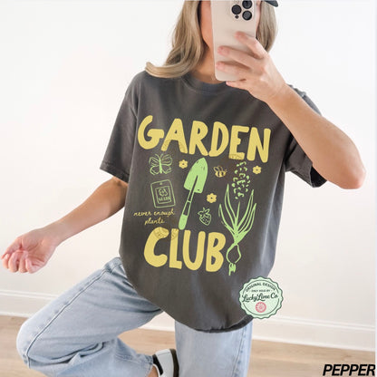 Person wearing a t-shirt with 'Garden Club' text and graphics, taking a mirror selfie.