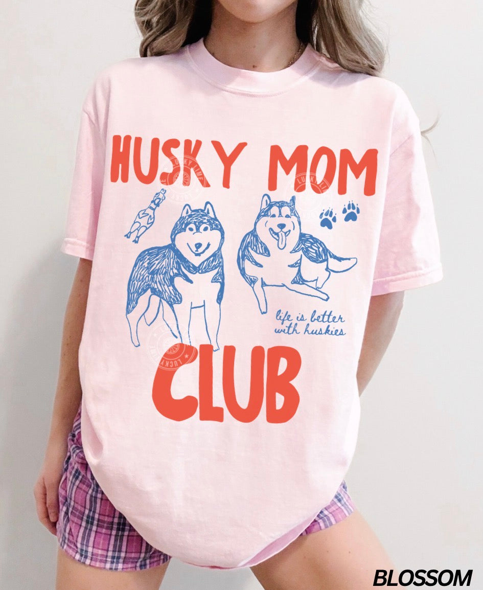 Person wearing a pink 'Husky Mom Club' t-shirt with dog graphics on a plain background
