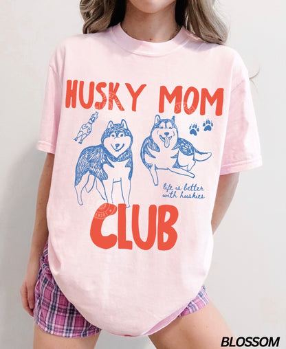 Person wearing a pink 'Husky Mom Club' t-shirt with dog graphics on a plain background