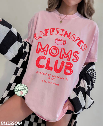 Person wearing a pink t-shirt with 'Caffeinated Moms Club' text, standing next to a black and white checkered garment.