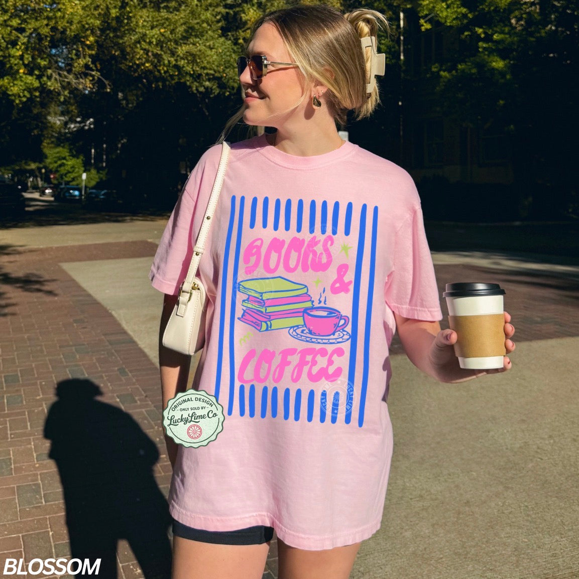 Person wearing a pink t-shirt with 'Books & Coffee' design, holding a coffee cup outdoors.