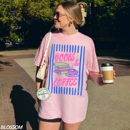 Person wearing a pink t-shirt with 'Books & Coffee' design, holding a coffee cup outdoors.