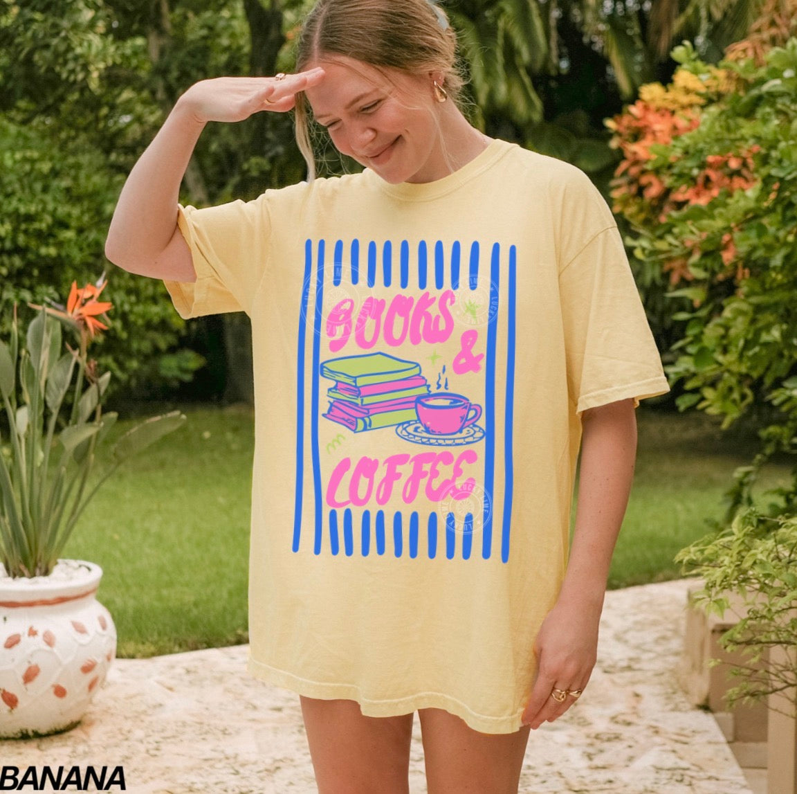 Person wearing a yellow t-shirt with 'Books & Coffee' design outdoors.