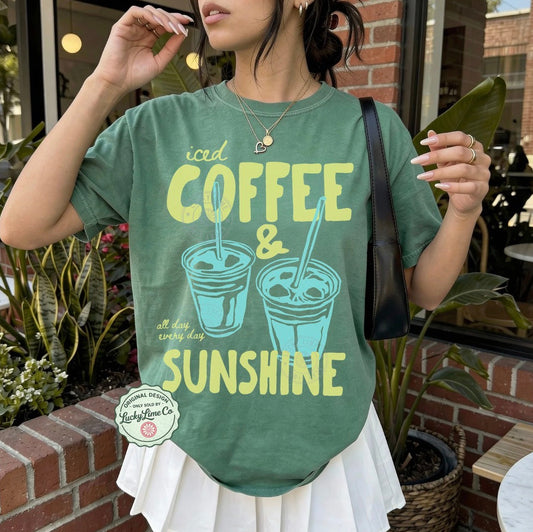 Person wearing a green t-shirt with 'iced coffee & sunshine' design outdoors.