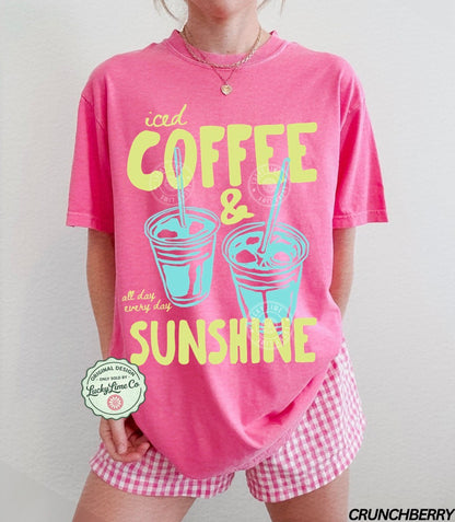 Person wearing a pink t-shirt with 'iced coffee & sunshine' text and checkered shorts on a plain background.