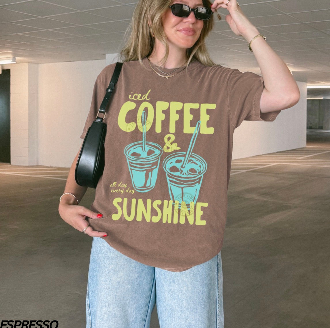 Woman wearing a brown t-shirt with 'iced coffee & sunshine' text and graphics.