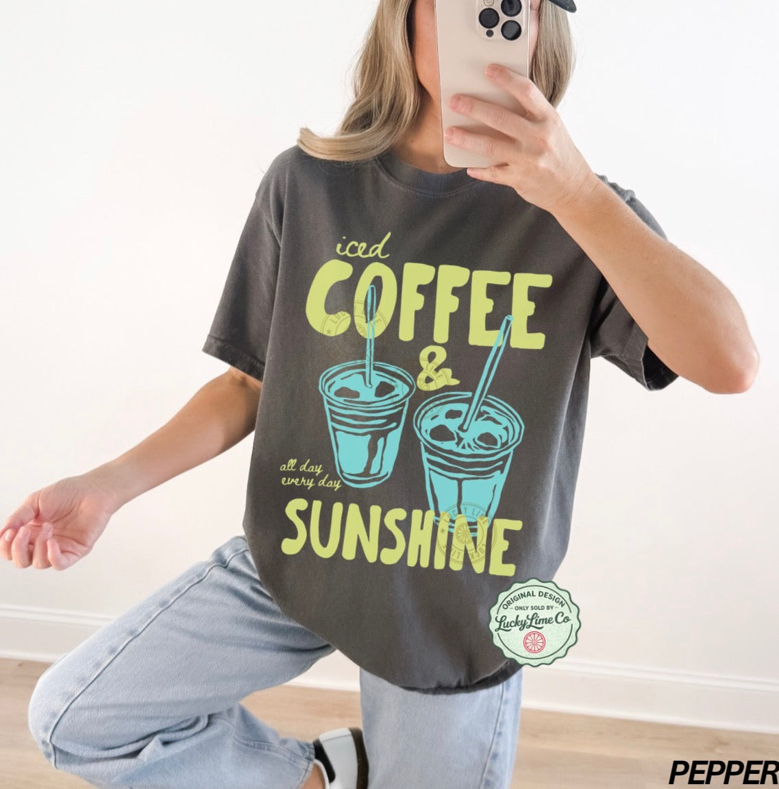 Person wearing a t-shirt with 'iced coffee & sunshine' design, taking a mirror selfie.