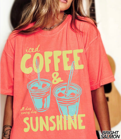 Person wearing a coral t-shirt with 'iced coffee & sunshine' text and graphics.