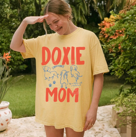 Woman wearing a yellow 'Doxie Mom' t-shirt outdoors.