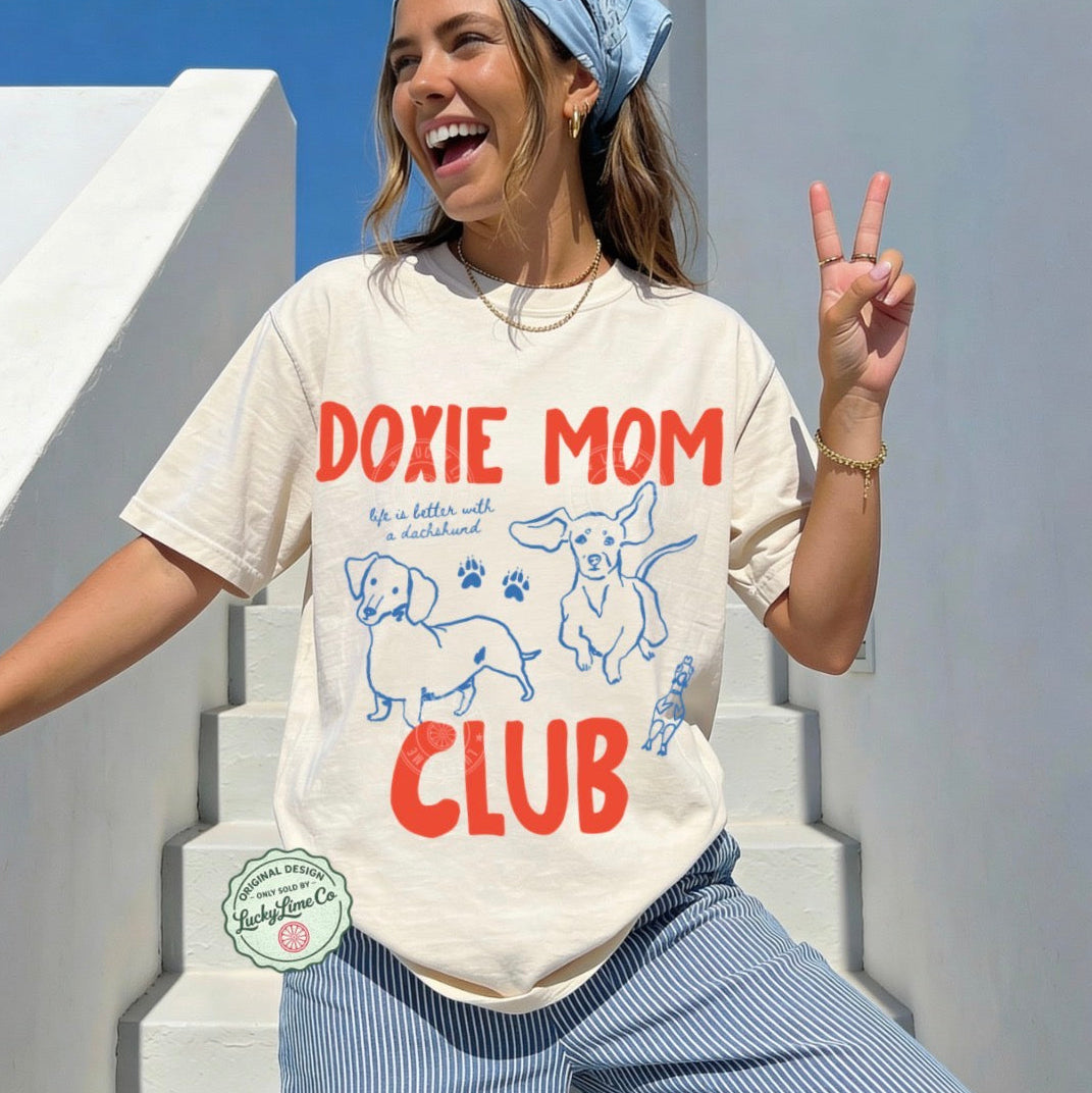 Woman wearing a 'Doxie Mom Club' t-shirt on a sunny day.