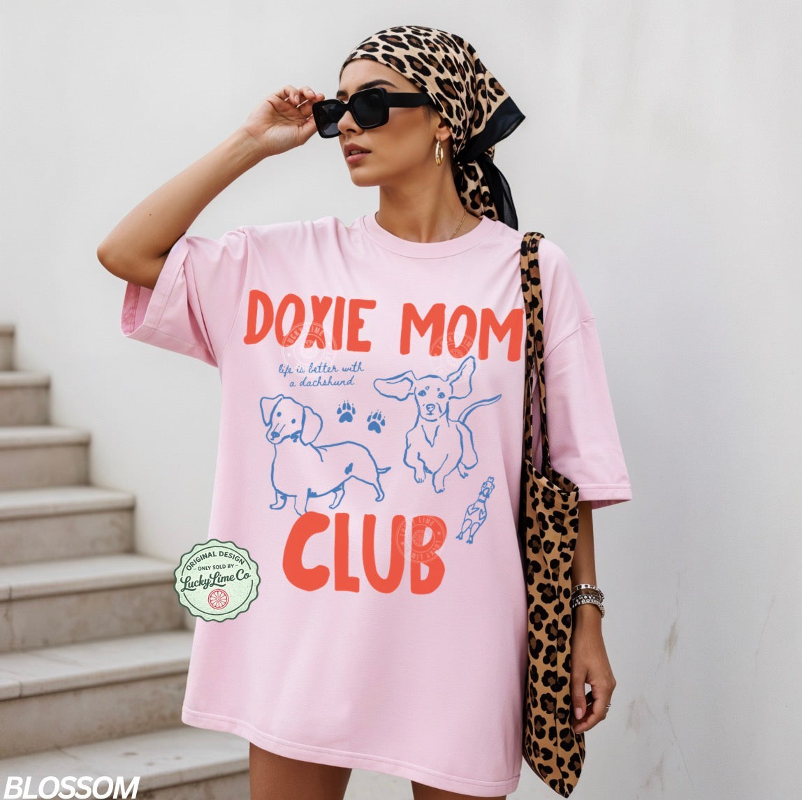 Woman wearing a pink 'Doxie Mom Club' t-shirt with a leopard print headscarf and bag.