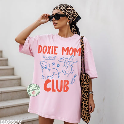 Woman wearing a pink 'Doxie Mom Club' t-shirt with a leopard print headscarf and bag.