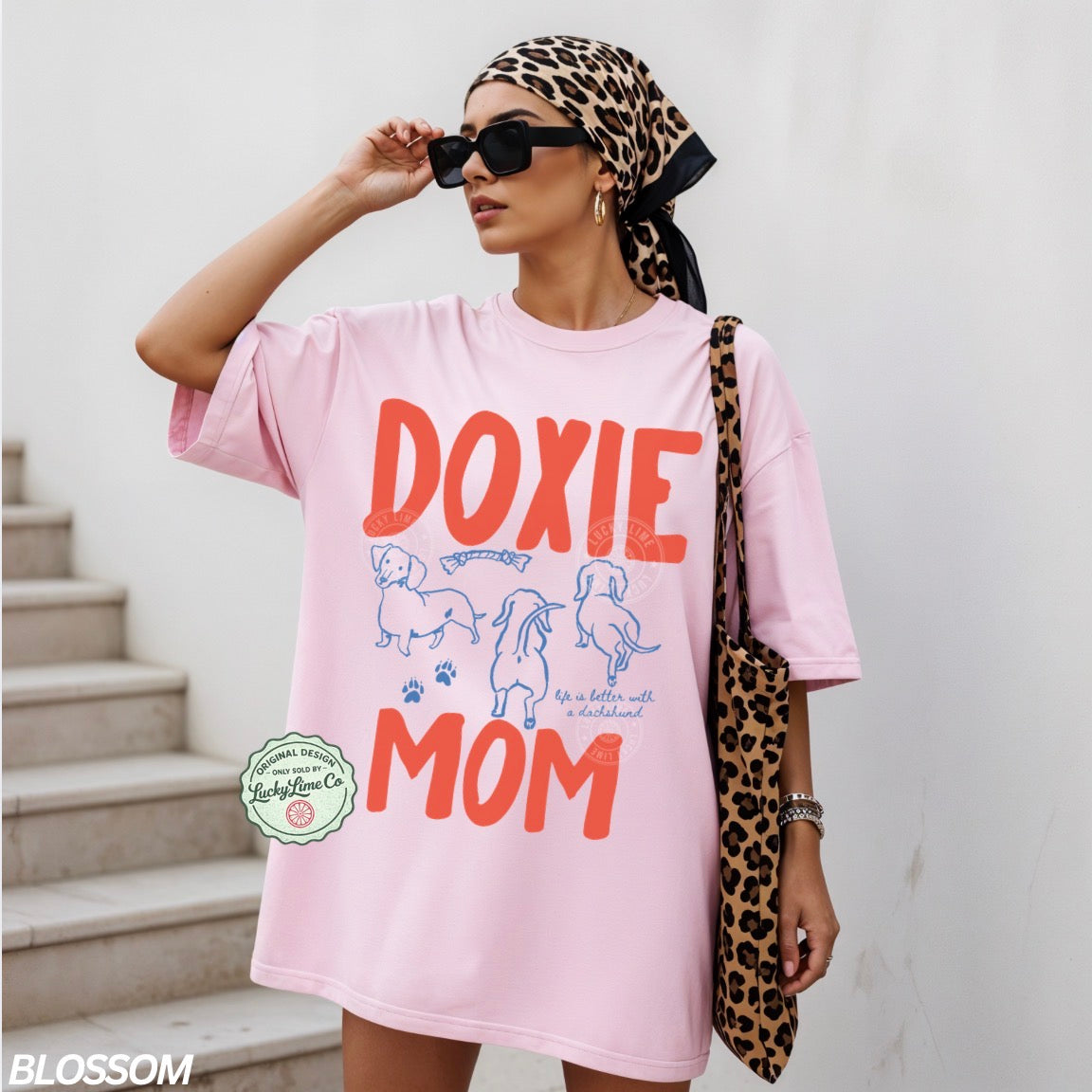 Woman wearing a pink 'Doxie Mom' t-shirt with a leopard print headscarf and bag.