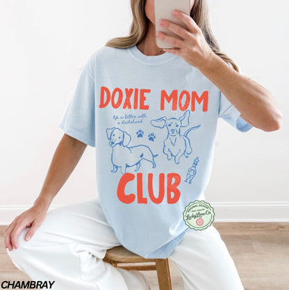 Person wearing a light blue t-shirt with 'Doxie Mom Club' text and dachshund illustrations.