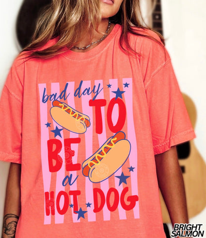 Person wearing a coral t-shirt with a hot dog graphic and text.