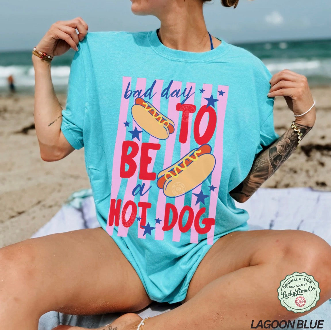Person wearing a light blue t-shirt with a colorful graphic and text on a beach.