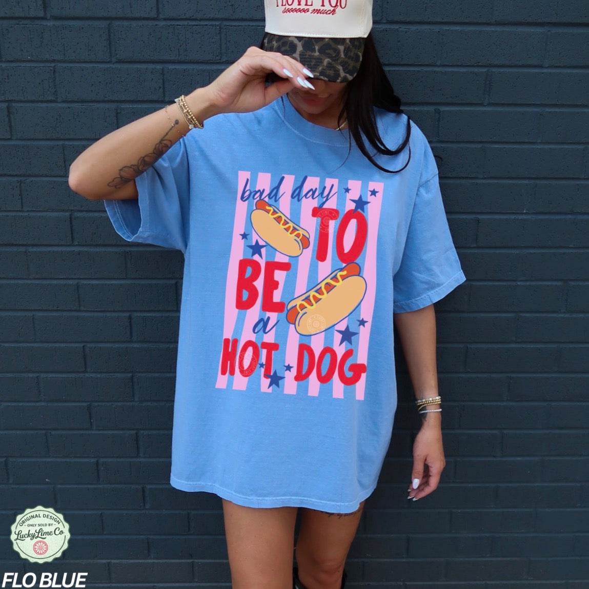 Person wearing a blue t-shirt with a hot dog graphic and text against a dark brick wall.
