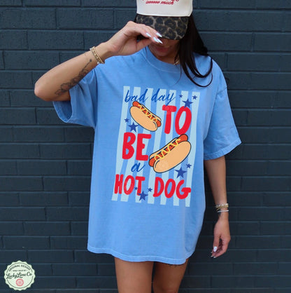 Person wearing a blue t-shirt with a hot dog graphic and text against a dark brick wall.