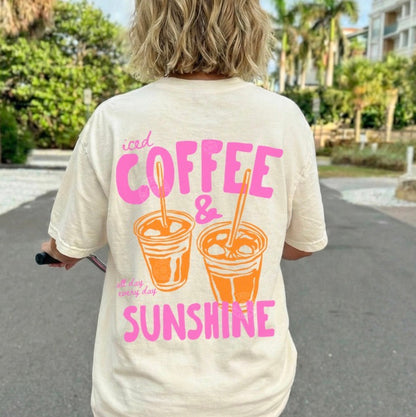 Person wearing a t-shirt with 'iced coffee & sunshine' text and graphics, riding a pink scooter outdoors.