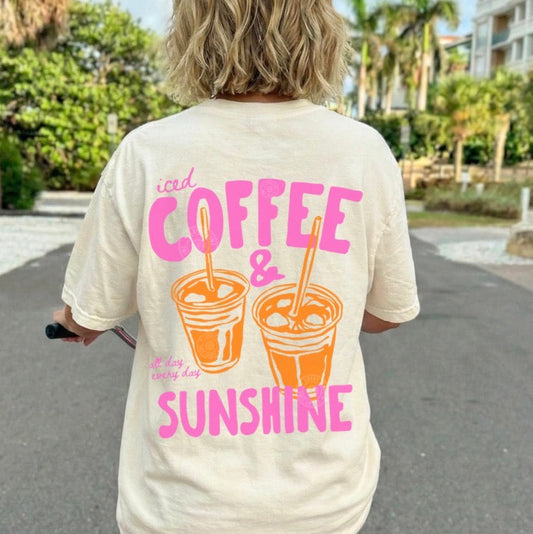 Person wearing a t-shirt with 'iced coffee & sunshine' text and graphics, riding a pink scooter outdoors.
