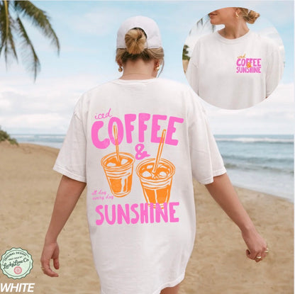 Woman wearing a white t-shirt with 'iced coffee & sunshine' design on a beach.