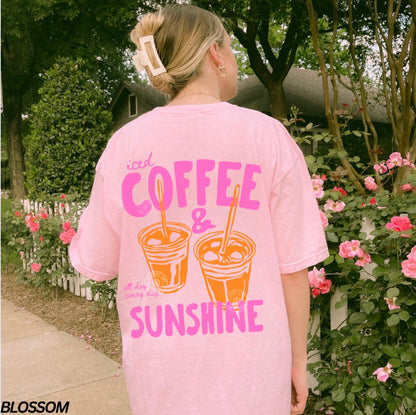 Person wearing a pink t-shirt with 'iced coffee & sunshine' design outdoors.