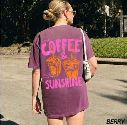 Person wearing a purple t-shirt with 'iced coffee & sunshine' text outdoors.