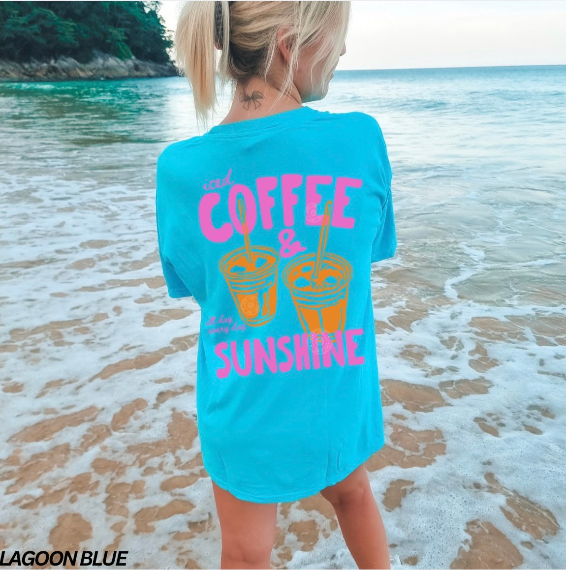 Person wearing a blue t-shirt with 'Coffee & Sunshine' text and graphics on a beach.