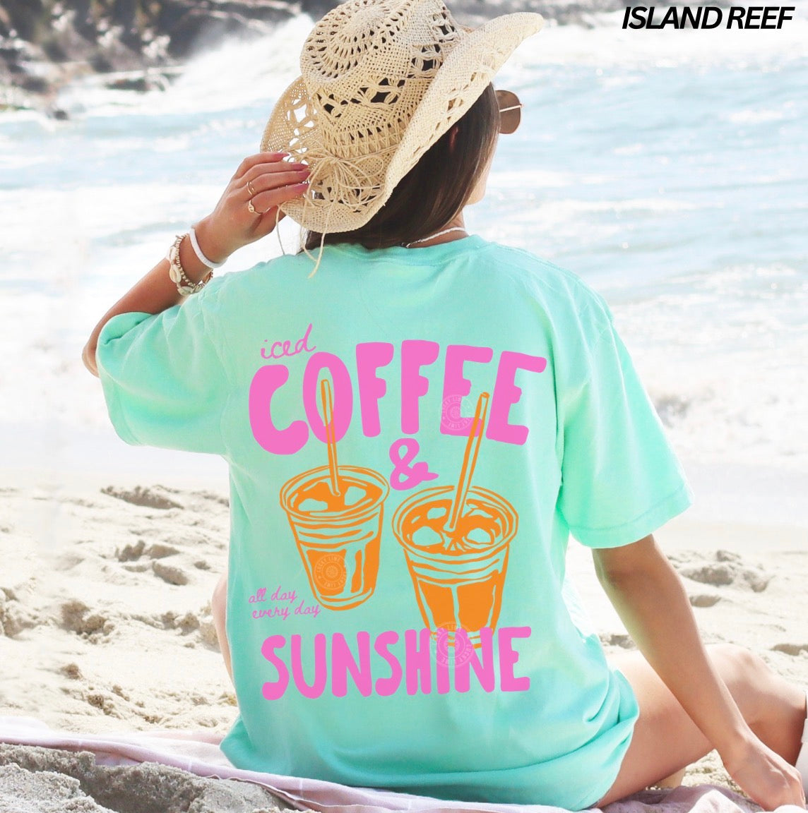 Person wearing a light blue t-shirt with 'iced coffee & sunshine' text on a beach.