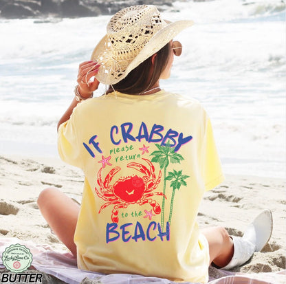 Person sitting on a beach wearing a yellow t-shirt with a crab and palm tree design.