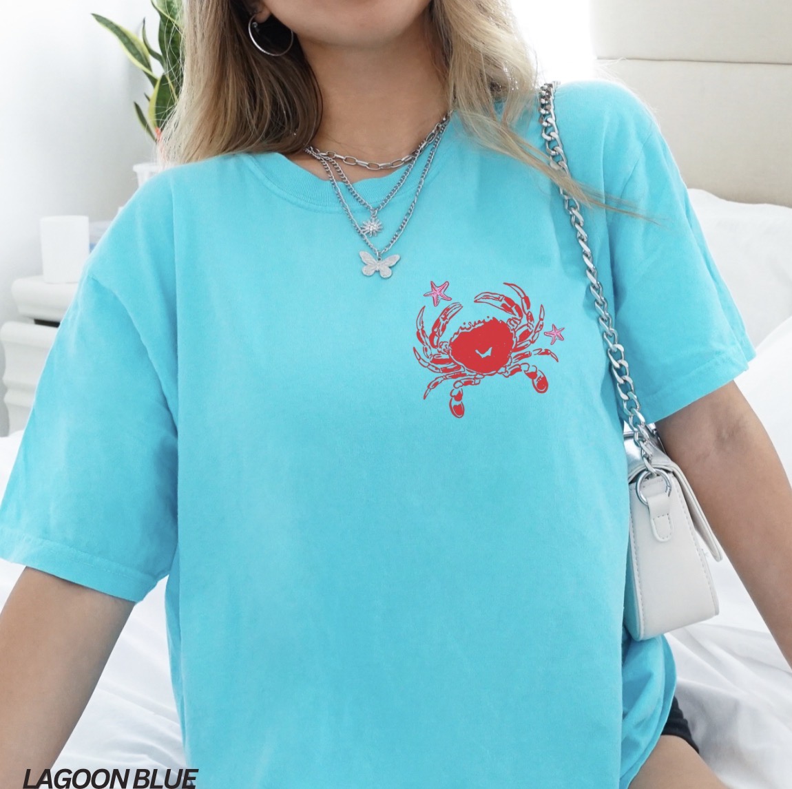 Person wearing a light blue t-shirt with a red crab design, sitting on a white couch.