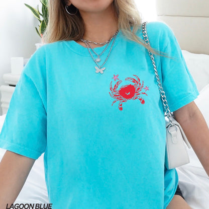 Person wearing a light blue t-shirt with a red crab design, sitting on a white couch.