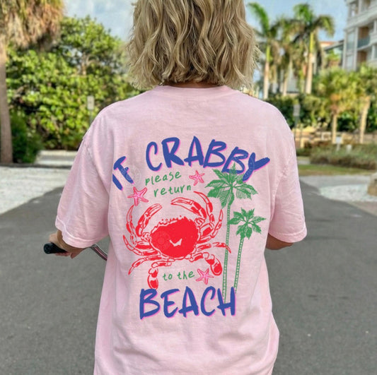 Person wearing a pink t-shirt with a beach-themed design and text, standing on a street.
