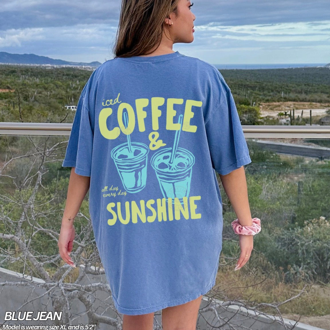 Person wearing a blue t-shirt with 'iced coffee & sunshine' text, standing outdoors.