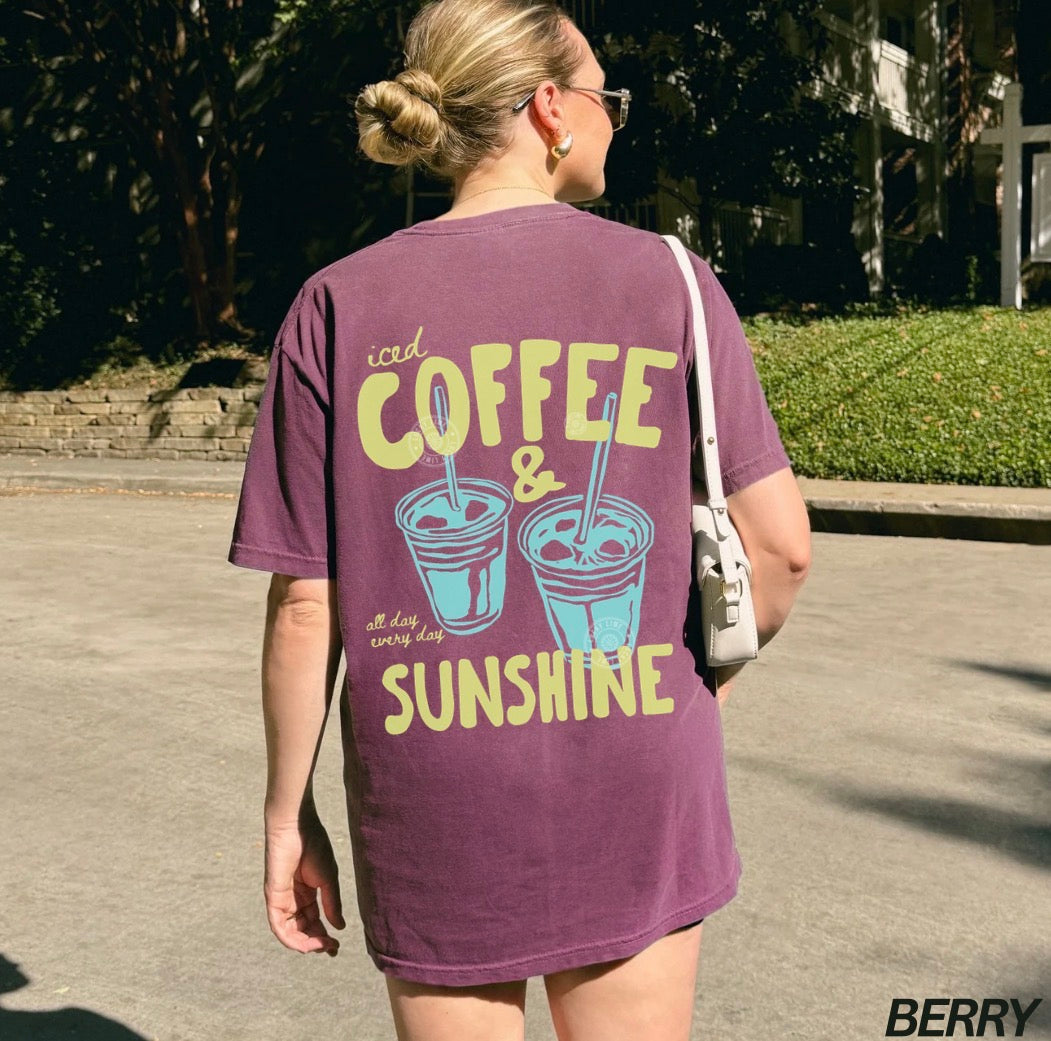 Person wearing a purple t-shirt with 'iced coffee & sunshine' text outdoors.