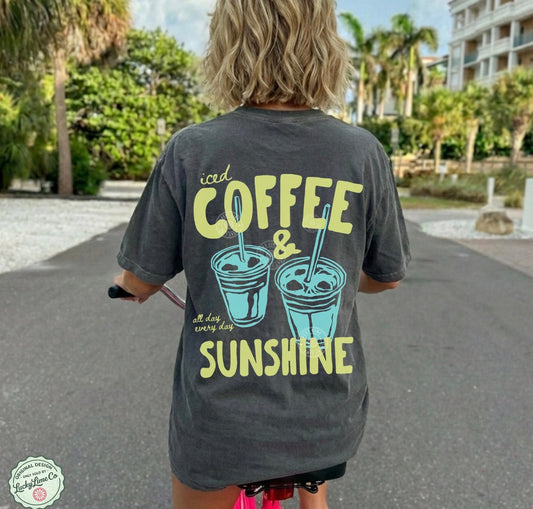 Person wearing a t-shirt with 'iced coffee & sunshine' text and graphics, riding a bike outdoors.