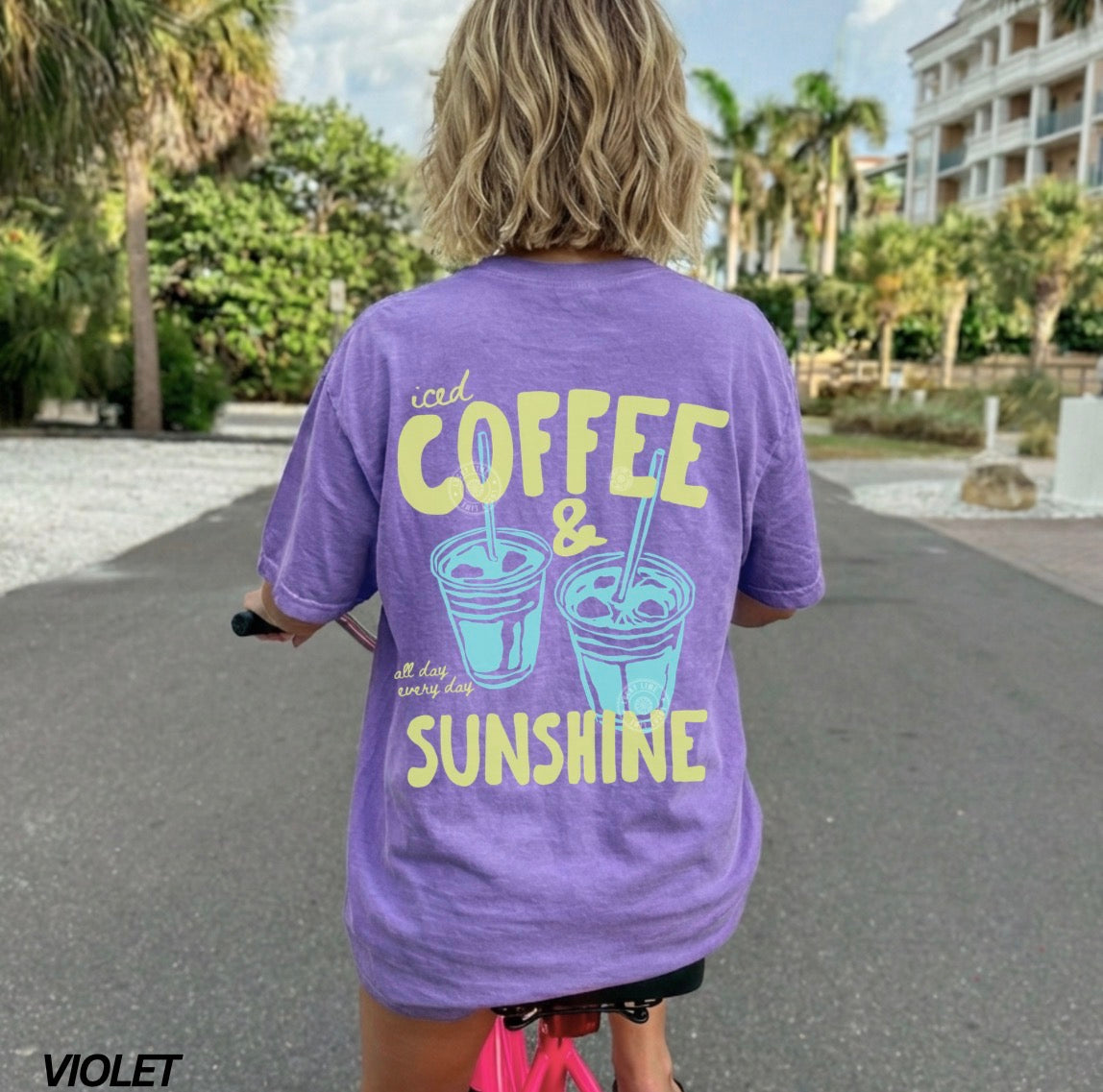 Person wearing a purple t-shirt with 'iced coffee & sunshine' text, standing outdoors.